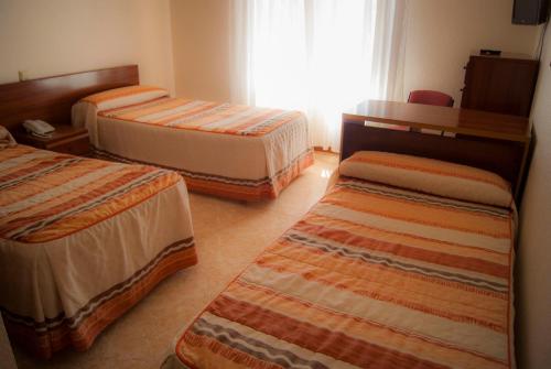a hotel room with three beds and a window at Hostal Hermanos Gutierrez in Monasterio de Rodilla