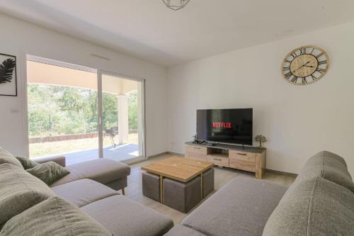 a living room with a couch and a tv and a clock at Charmante maison 6 à 8 pers PMR proche Lyon in Seyssuel