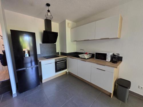 une cuisine avec des armoires blanches et un réfrigérateur noir dans l'établissement T2 avec parking aux portes de montpellier, à Castelnau-le-Lez