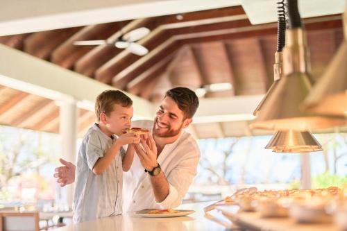 a man and a boy eating pizza at a table at The Westin Reserva Conchal, an All-Inclusive Golf Resort & Spa in Playa Conchal