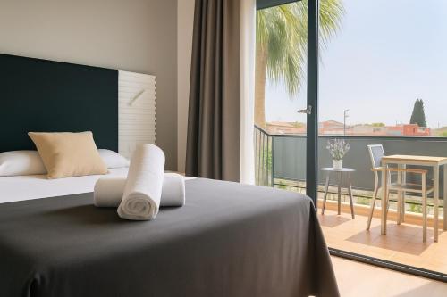 a bedroom with a bed and a balcony with a table at Hotel Sitges in Sitges