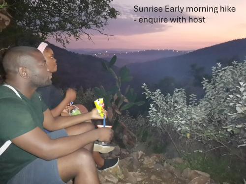 a man and a young woman sitting on a hill looking at the sunset at Rustic Unique - Bush Glamping Retreat in Kalkheuvel