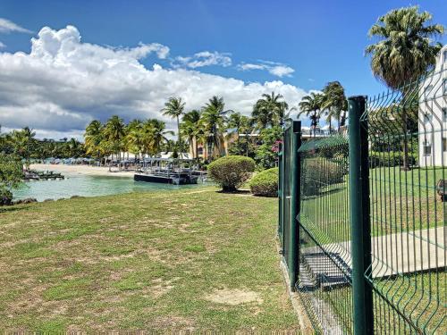 a fence next to a body of water with palm trees at Appartement bord de mer très fonctionnel -accès direct plage & Vue mer exceptionnelle in Le Gosier