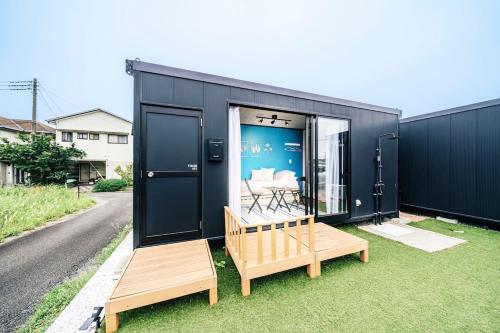 a black tiny house with two benches on the grass at T-Base 01 in Tateyama