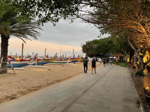people walking down a sidewalk on the beach with boats at Oasis Residences in Sanur