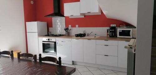 une cuisine avec des placards blancs et un mur rouge dans l'établissement Maison au cœur du Sancy, à Férérolles