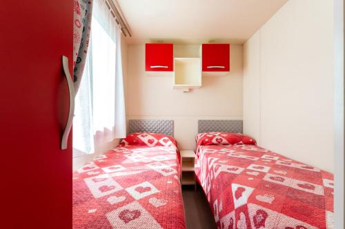 two beds in a small room with red cabinets at Villaggio San Francesco - Adria Holiday Mobile Homes in Duna Verde
