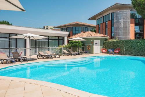 a swimming pool with chairs and umbrellas next to a building at Appart'City Confort Toulouse Purpan in Toulouse