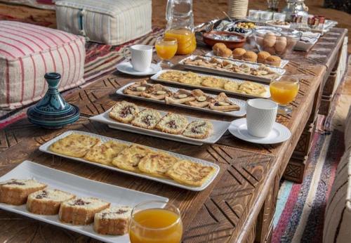 een tafel bedekt met schalen vol gebak en sinaasappelsap bij Merzouga Glossy Camp in Merzouga
