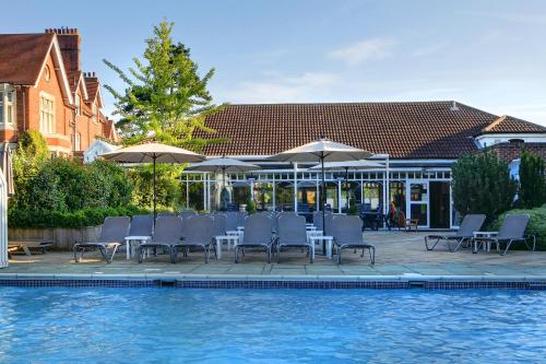 a group of chairs and umbrellas next to a swimming pool at Pontlands Park Hotel in Chelmsford