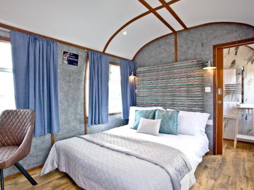 a bedroom with a bed with blue curtains and a chair at Brunel Boutique Railway Carriage 4 in Dawlish Warren