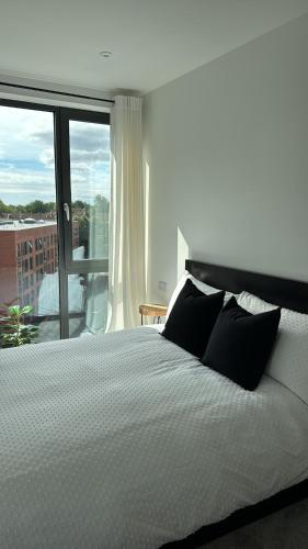 ein Bett mit schwarzen Kissen in einem Schlafzimmer mit Balkon in der Unterkunft Salford Luxury 2Bed 2Bath Gym Balcony in Manchester