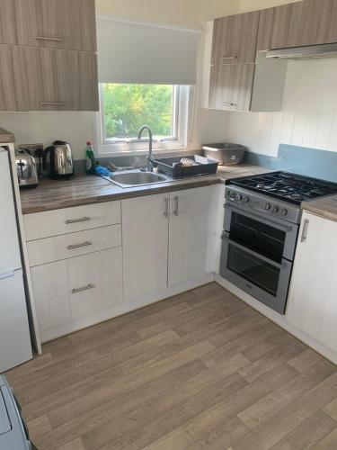 a kitchen with white cabinets and a sink and a stove at Beautiful beach themed static caravan in Hastings
