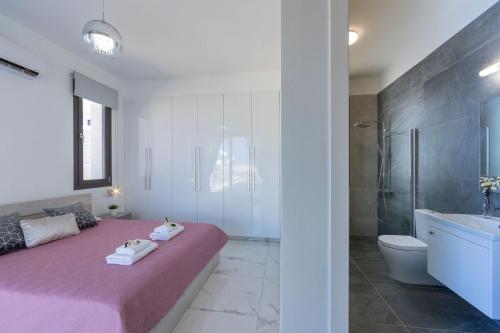 ein Schlafzimmer mit einem rosa Bett und ein Badezimmer in der Unterkunft Luxury Paphos Villa Villa Adaris 5 Bedroom Villa Private Swimming Pool in Peyia