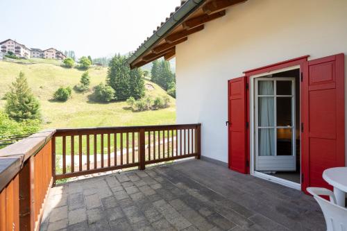 a balcony with a red door and a table at Dolomites Hotel La Meridiana in Moena