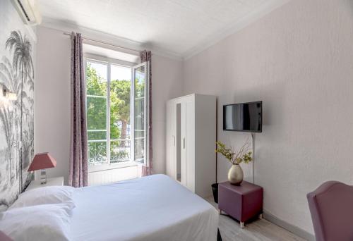 a white bedroom with a bed and a window at Hotel Les Palmiers in Sainte-Maxime