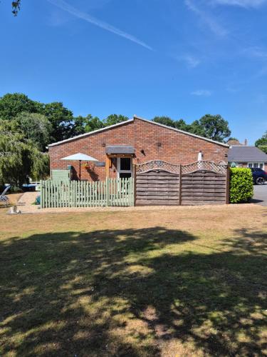 a brick building with a fence and an umbrella at The Woodpeckers - Alresford Essex in Alresford