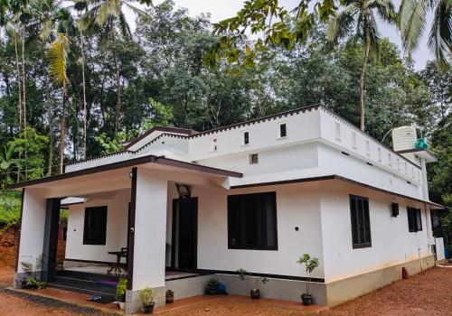 a white house with trees in the background at Gods Gift Homestay James Inn in Kozhikode