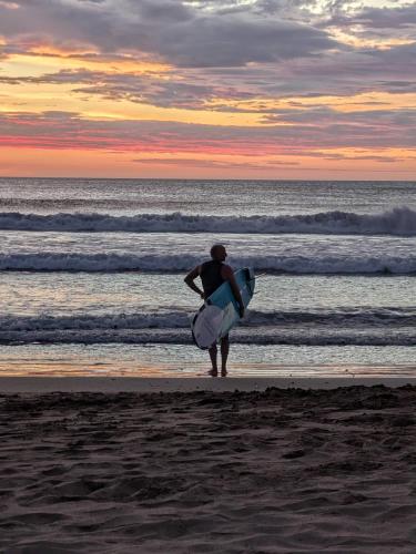 a man walking on the beach holding a surfboard at Seis Playas Hotel in Tamarindo