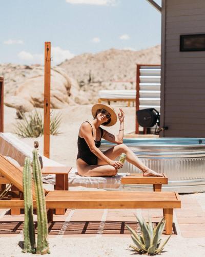 a woman in a hat sitting next to a pool at Fox Inn Epic Views, Hot Tub, Cowboy Tub, Grill in Yucca Valley
