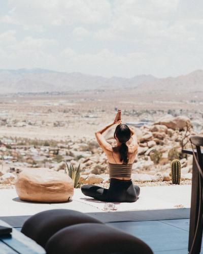 a woman sitting in a yoga position looking out at the desert at Fox Inn Epic Views, Hot Tub, Cowboy Tub, Grill in Yucca Valley