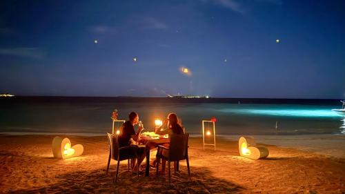 two people sitting at a table on the beach at night at Belmar Beach in Bodufolhudhoo