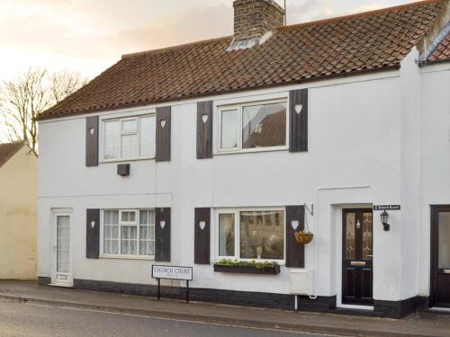a white house with black windows and a sign at Church Court Cottage in Beeford