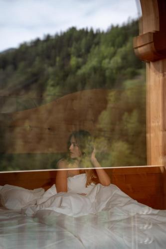 a woman laying in bed looking out a window at Naturhotel Lüsnerhof in Luson