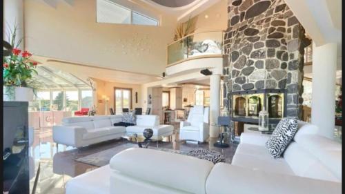 Il comprend un salon doté d'un mobilier blanc et d'une cheminée en pierre. dans l'établissement Lakefront Wellness Estate - Pool, Sauna and Hot Tub, à Lac-Simon