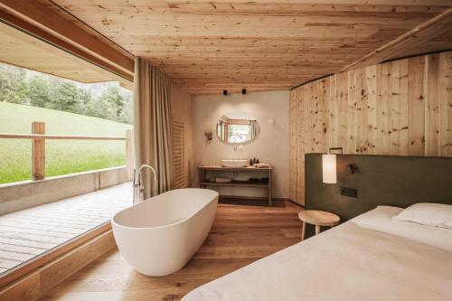 a bedroom with a tub and a bed and a window at Naturhotel Lüsnerhof in Luson