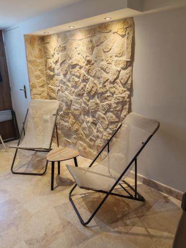 two chairs and a table in front of a stone wall at Gîte Drôme des collines in Anneyron