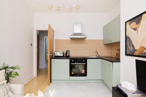 a kitchen with white cabinets and a stove top oven at The Camden Hideout - Modish and Bright 2BDR Flat in London