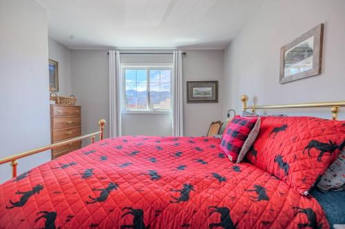 a bedroom with a bed with a red comforter and a window at The Riverside Retreat at Fairmont in Fairmont Hot Springs