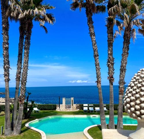 a pool with palm trees and the ocean at Villa Seba Sicily in Augusta