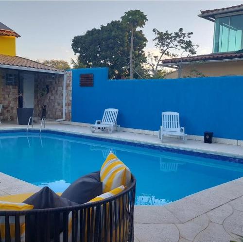 a swimming pool with two chairs and a blue wall at Pousada Summer Beach by Itaúna in Saquarema
