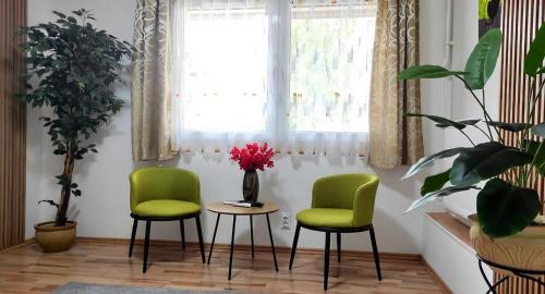 a room with two green chairs and a table and a window at Clementine Apartman in Százhalombatta