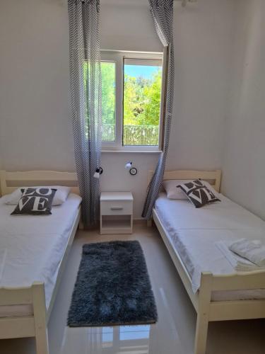two beds in a room with a window and a rug at Apartmani Ana i Mia in Ston