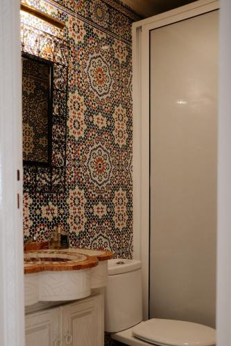 a bathroom with a toilet and a tile wall at Riad Searenity in Tamraght Ouzdar