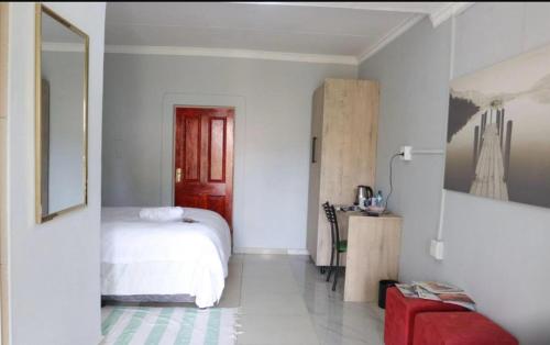 a white bedroom with a bed and a red stool at 54 River Logde in Mokopane