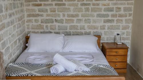 a bed with white sheets and pillows next to a brick wall at Ballkoni i Goricës in Goricë