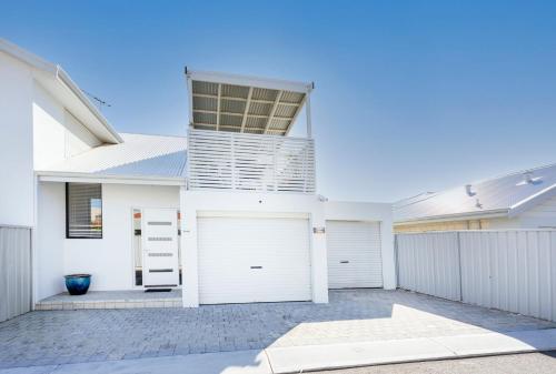 a white house with two garage doors and a fence at Scarborough Villa on Mickey in Perth