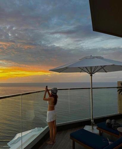 a woman standing on a balcony looking out at the ocean at Apec Mandala Harmony Resort & Spa in Mui Ne
