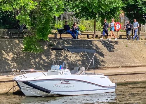 a boat is docked in the water with people sitting on a bench at York Marina in Naburn