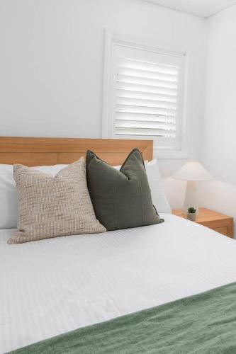 a bed with three pillows on top of it at 'Bulli Escape' Bright Beachfront Stay & Scenic Views in Bulli