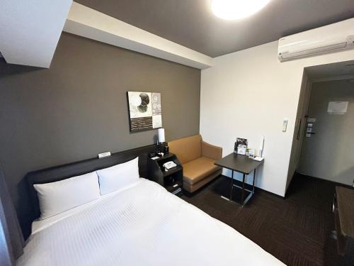 a bedroom with a bed and a chair and a table at Hotel Route Inn Toyama Inter in Toyama