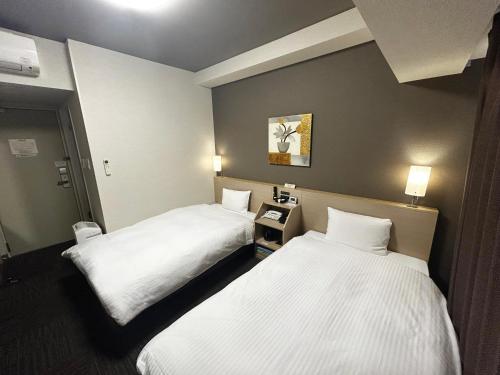 two beds in a hotel room with white sheets at Hotel Route Inn Toyama Inter in Toyama