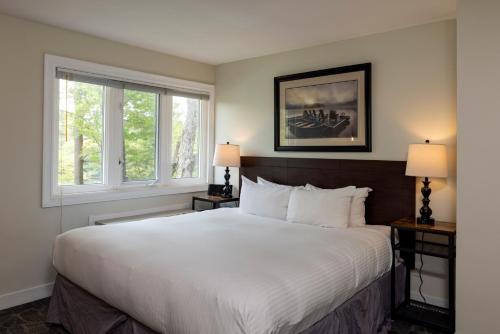 Un dormitorio con una gran cama blanca con dos ventanas. en Rocky Crest Golf Resort, en MacTier