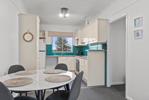 グレネルグにあるBeachside 2-Bed Apartment with Balcony Viewsの白いキャビネットとテーブルと椅子のあるキッチン