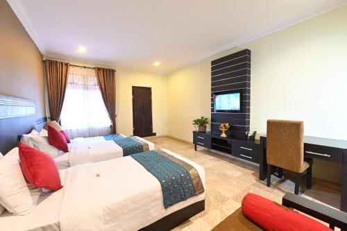 a bedroom with two beds and a desk and a television at Puri Dewa Bharata Hotel & Villas in Legian