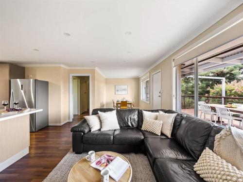 a living room with a black leather couch and a kitchen at Eagle Bay Beach House - 300m to the beach! in Dunsborough